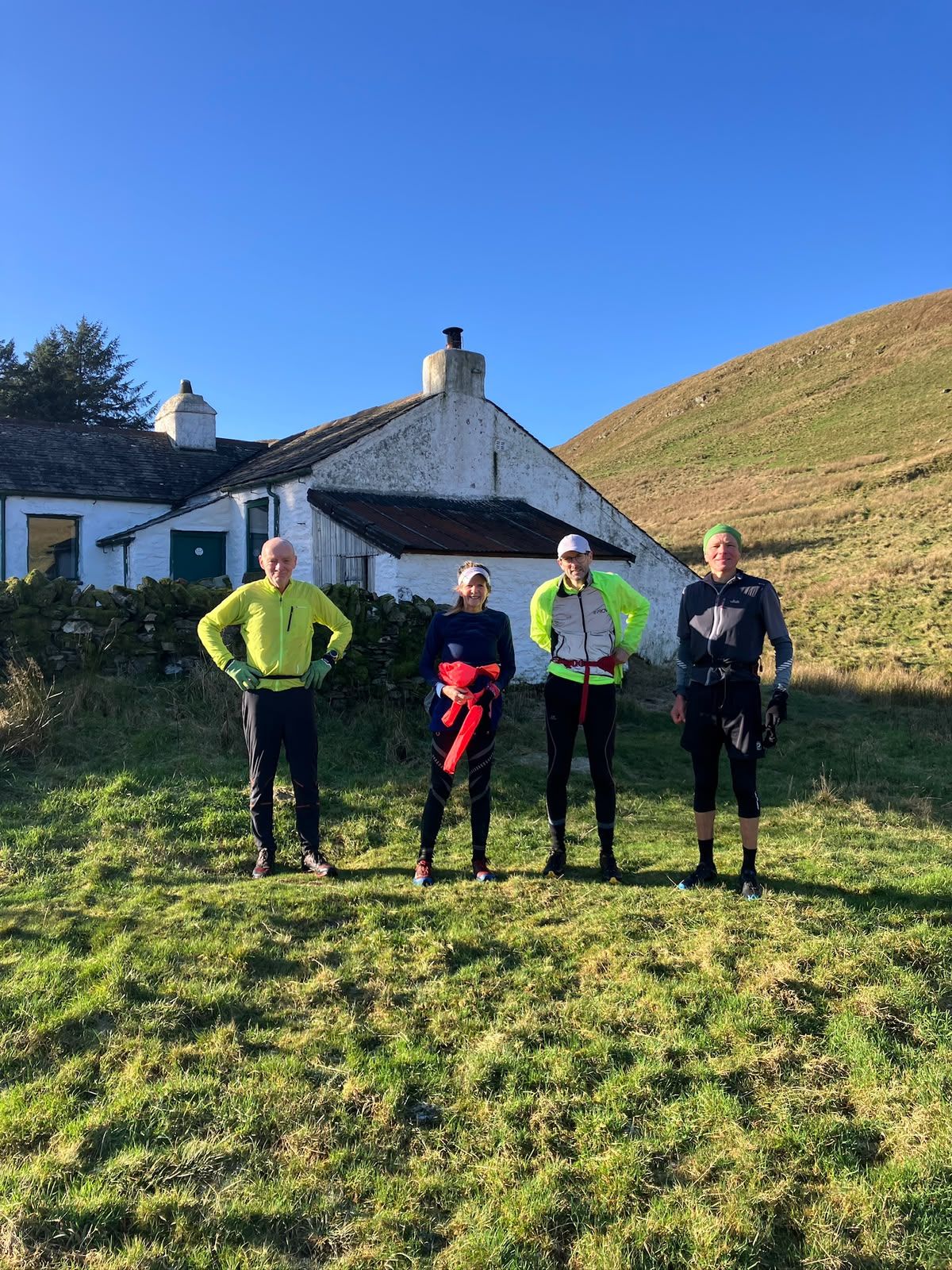 Four runners stand outside a small white cottage on the open fell.