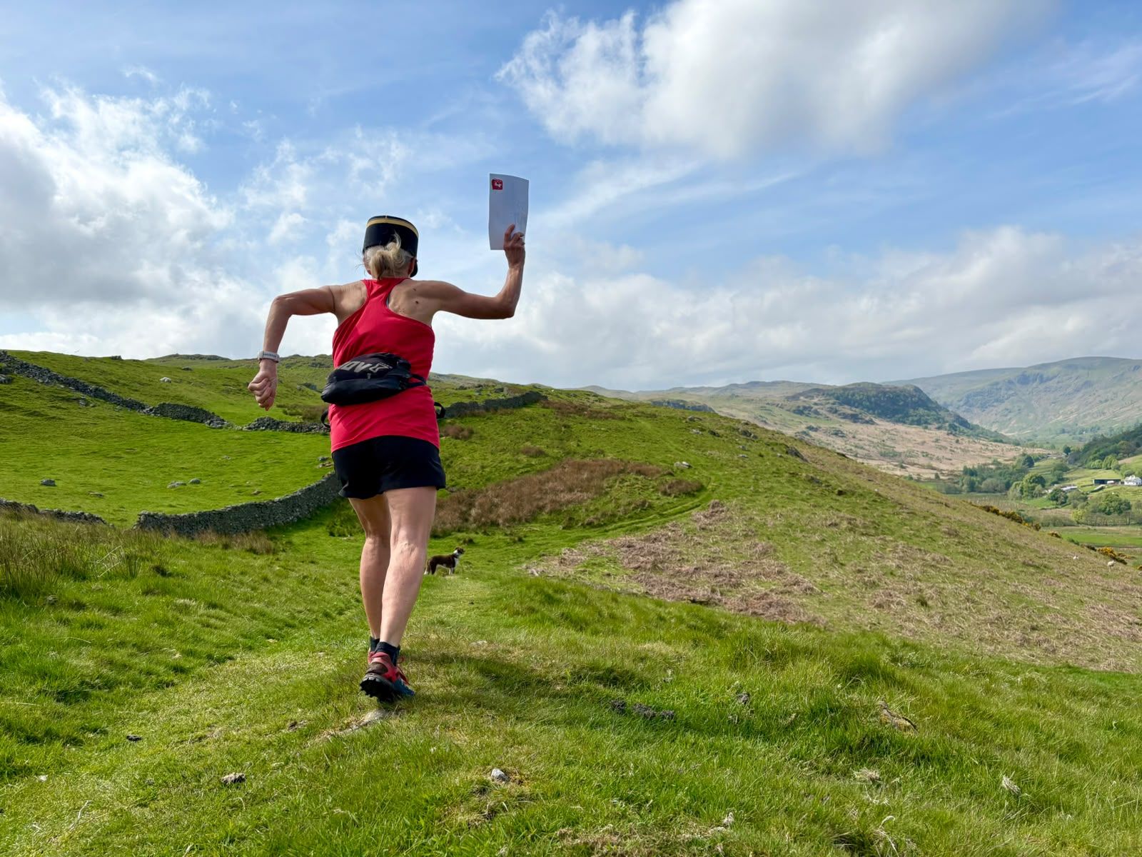 A runner in a postie’s cap leaps along a grassy ridge holding a letter aloft.