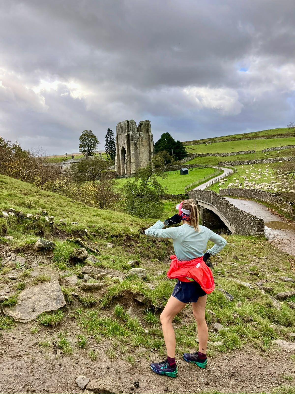 A runner photographs the tower of Shap Abbey beside an old stone bridge.