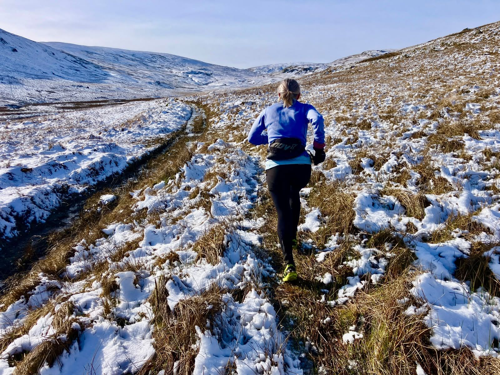 A runner on a snowy fell track under a pale sky.
