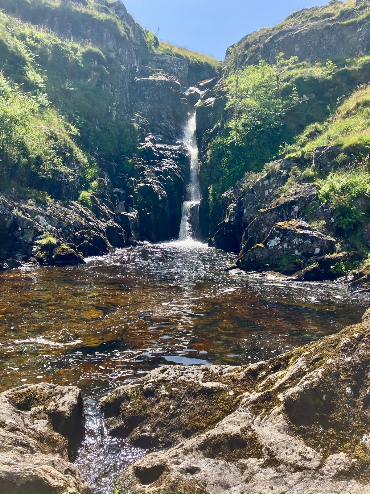 A tall waterfall pours into a dark pool between mossy crags.